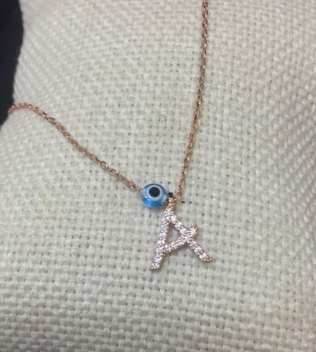 Close-up image of a personalized initial "A" necklace with cubic zirconia detailing and an evil eye charm, crafted in 18K gold-plated sterling silver.