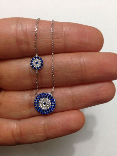 Double evil eye necklace with blue and clear cubic zirconia stones, handmade from 925 sterling silver, featuring a unique and protective design.