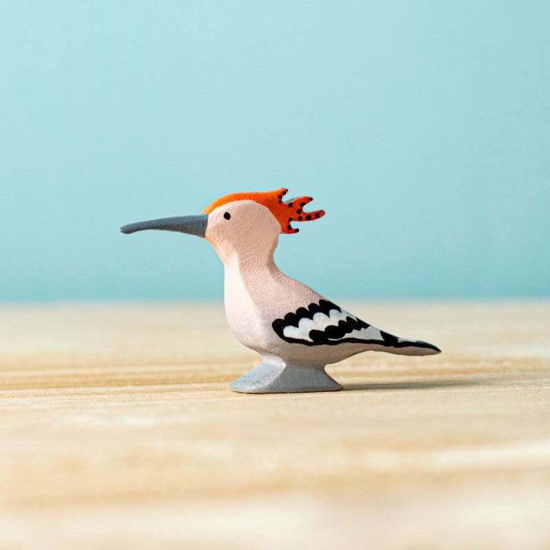 Image of the BumbuToys Hoopoe bird standing on a natural wooden table, sunlight illuminating its colorful crest.