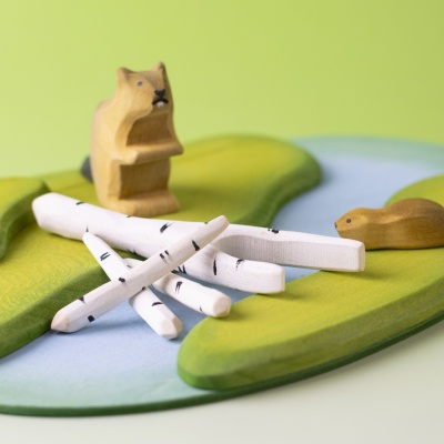 Birch branches in a beaver dam play scene with green and blue felt landscape.