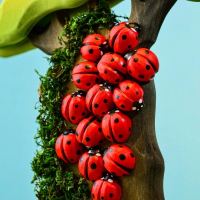 A collection of red wooden ladybug toys climbing a tree trunk with green leaves, creating a lively and playful scene.