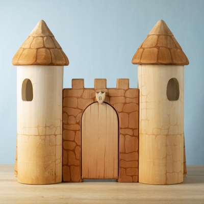 Wooden toy castle with two towers and central gate on a wooden surface.