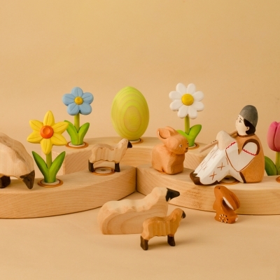 Wooden pastoral scene with sheep, bunnies, a traditional flute player, and spring flowers including a yellow daffodil