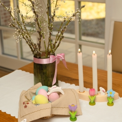 Festive spring table setup featuring wooden celebration ring, lit candles, and a basket of pastel eggs