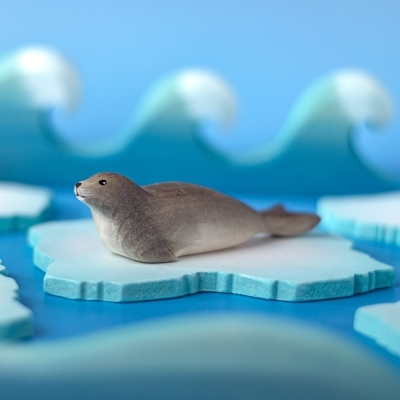 Handcrafted wooden seal figure resting on a blue wooden ice floe toy against a wave background.
