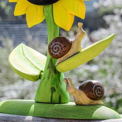 Close-up of two wooden snails on a large sunflower leaf, handmade by Bumbu Toys
