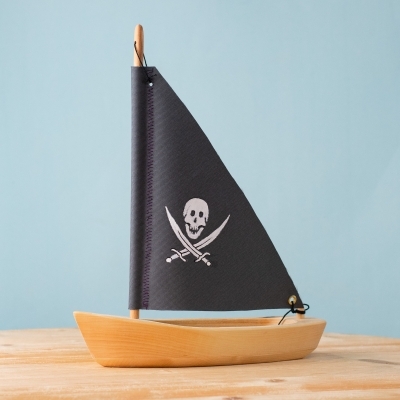 Handmade wooden Pirate Sailing Boat with black skull sail on wooden table.