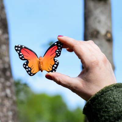 Hand holding a wooden butterfly toy against a natural background