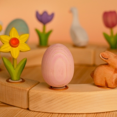 Pink wooden egg resting in a celebration ring next to a small brown bunny toy