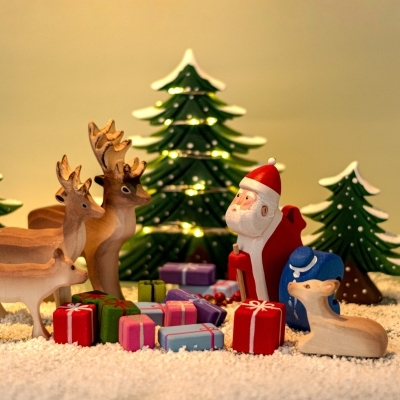 Wooden Reindeer Calf standing next to a wooden Santa Claus figure in a festive holiday display with Christmas trees.