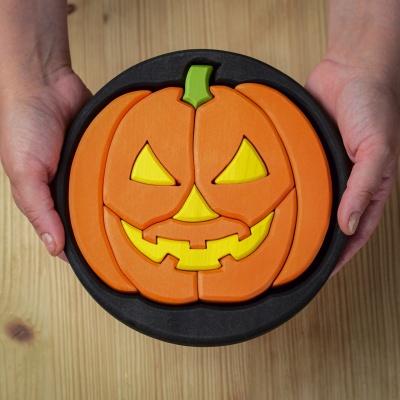 Hands holding a small handcrafted wooden round Halloween puzzle.