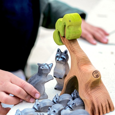 Close-up of a child arranging handcrafted wooden raccoon toys around a tree by Bumbu Toys