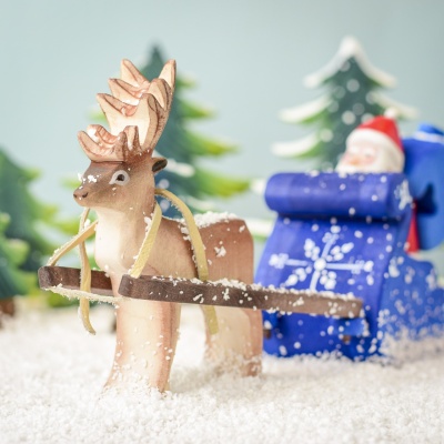 Wooden reindeer pulling a sled in a snowy forest setting.