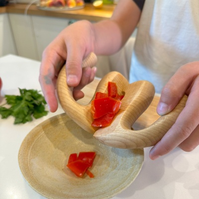 Child using the wooden salad spatula to scoop chopped red pepper