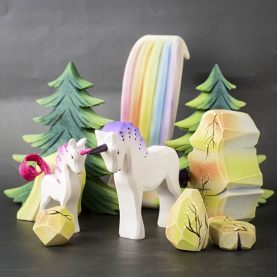 Two wooden unicorns in a magical landscape with a rainbow waterfall and nature elements.