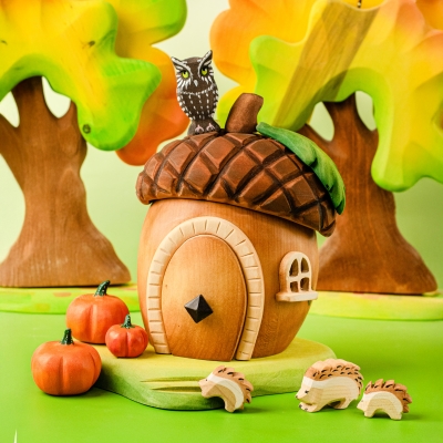 Child playing with a wooden acorn house, pink fairy, and white bunny toys on a play mat