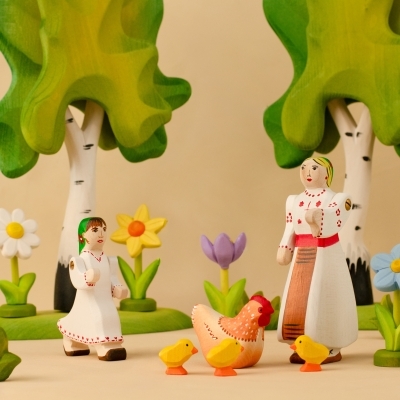 Spring play scene with traditional wooden dolls, a hen, chicks, birch trees, and a bright yellow toy daffodil
