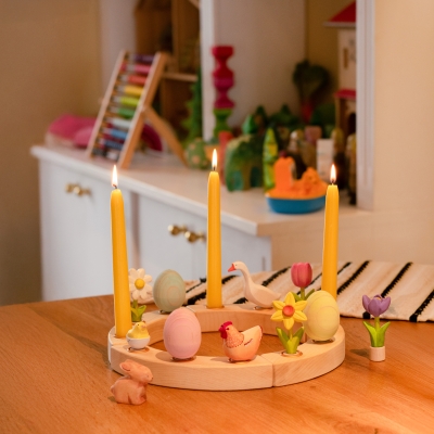 Lit candles in a wooden Waldorf ring decorated with a hen, chick, goose, and blue forget-me-not
