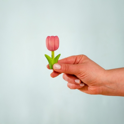 Hand holding a small pink wooden toy tulip showing its size and smooth painted finish