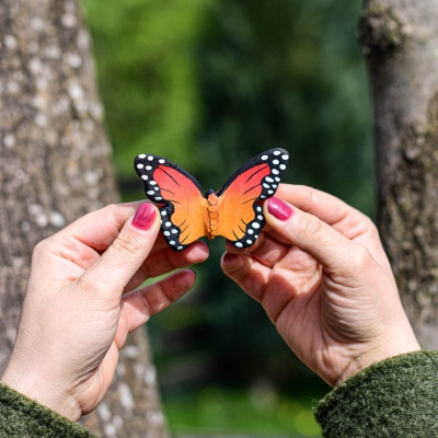 Hands holding a wooden butterfly toy against a green natural background