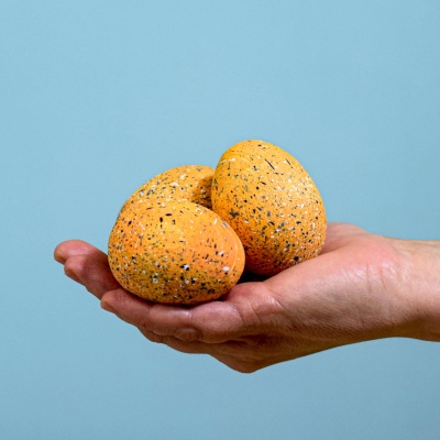 Hand holding three wooden Parasaurolophus eggs against a blue background.