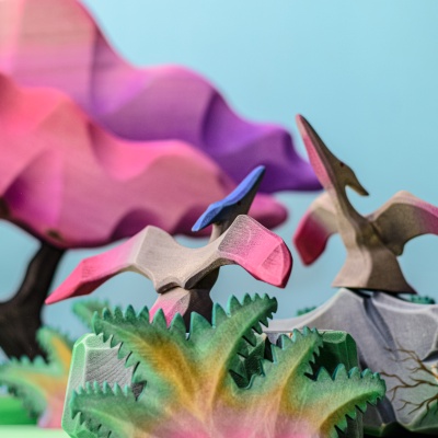 Two Pteranodons flying among colorful trees in a prehistoric scene.
