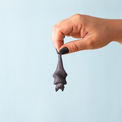 Handmade wooden bat toy hanging upside down held by hand.