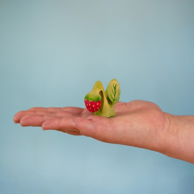 Adult hand holding the small 4.5cm wooden Strawberry Plant toy to demonstrate its compact size.