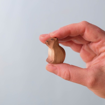 Small wooden baby capybara sitting, held between fingers, showing its size.