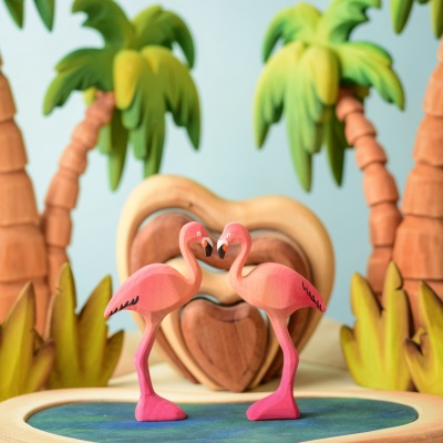 Pair of Flamingos in a play scene with palm trees and a heart-shaped backdrop.