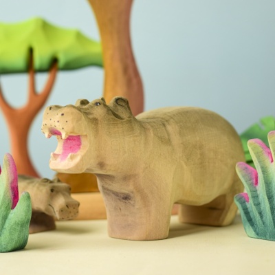 Two wooden Hippo toys with background trees and plants.