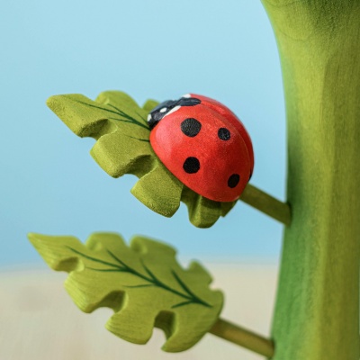 Close-up of a red and black wooden ladybug toy on a green leaf, showcasing intricate paint details and craftsmanship.
