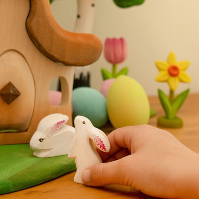 Child hand playing with wooden bunny toys near a fairy house and a pink handmade wooden tulip