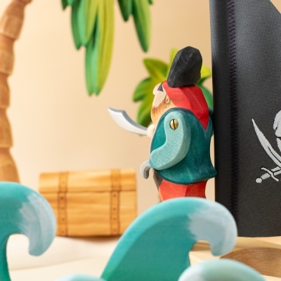 Pirate figure standing next to wooden Pirate Sailing Boat with treasure chest and palm tree.