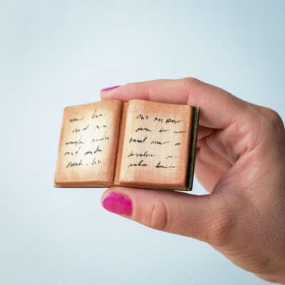 Hand holding a small handcrafted wooden open spellbook with hand-painted magical writings.