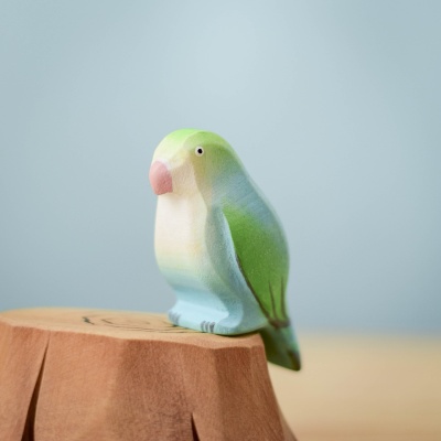 Blue Lovebird wooden toy sitting on a wooden stump, hand-painted in calming pastel blue and green tones.