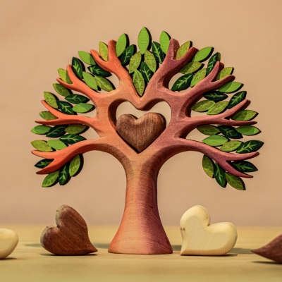 A wooden tree with green leaves and a red heart shape carved into its trunk. It sits on a brown stand.