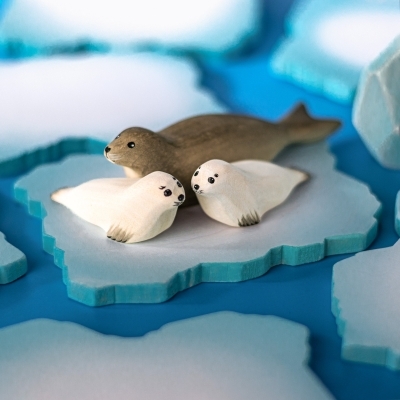 Adult wooden seal toy protecting two white seal pups on a blue ice floe base.