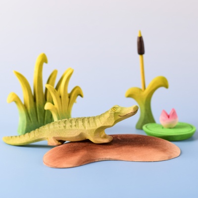 Baby crocodile on wooden island surrounded by reeds