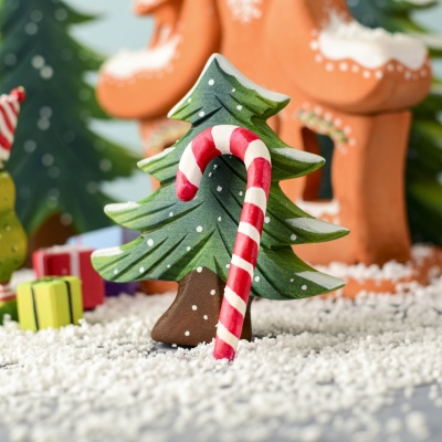 Handcrafted Wooden Candy Cane leaning against a Snowy Fir Tree in a festive Christmas scene.