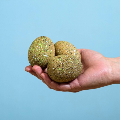 Hand holding three wooden Ankylosaurus eggs against a blue background.