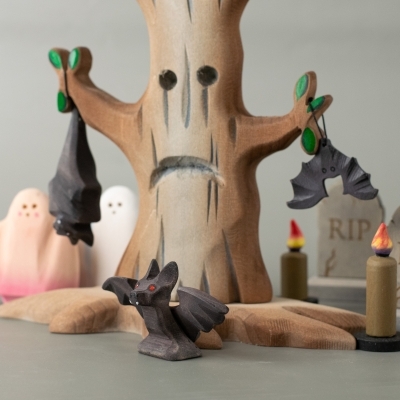Wooden bat toys displayed with ghost figures, tree, and candles in a Halloween scene.