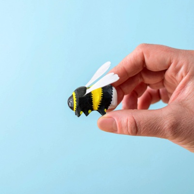 Hand holding a wooden bumblebee toy against a blue background