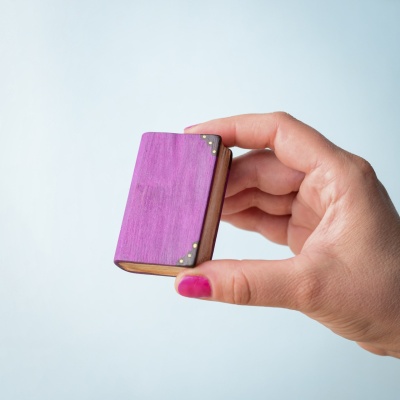 Hand holding a large handcrafted wooden book with a purple cover.