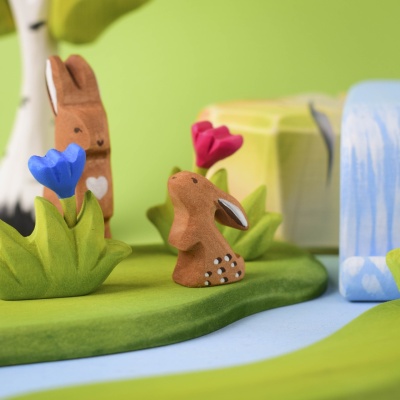 Wooden rabbit exploring a forest playset with flowers