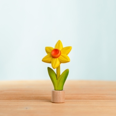 Single yellow handcrafted wooden toy daffodil standing upright on a light wood tabletop