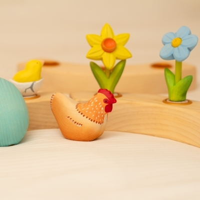 Close up of a wooden hen, chick, daffodil, and blue toy forget-me-not in a celebration ring