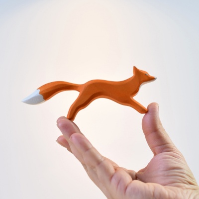The wooden fox toy standing next to a child's hand for size comparison.