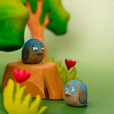Close-up of two small wooden bluebirds resting on a wooden stump in a play scene.