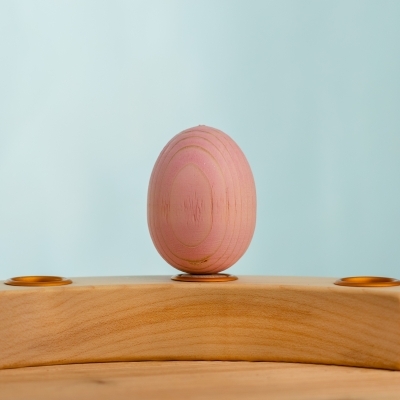 Pastel pink wooden toy egg placed carefully in a wooden Waldorf celebration ring